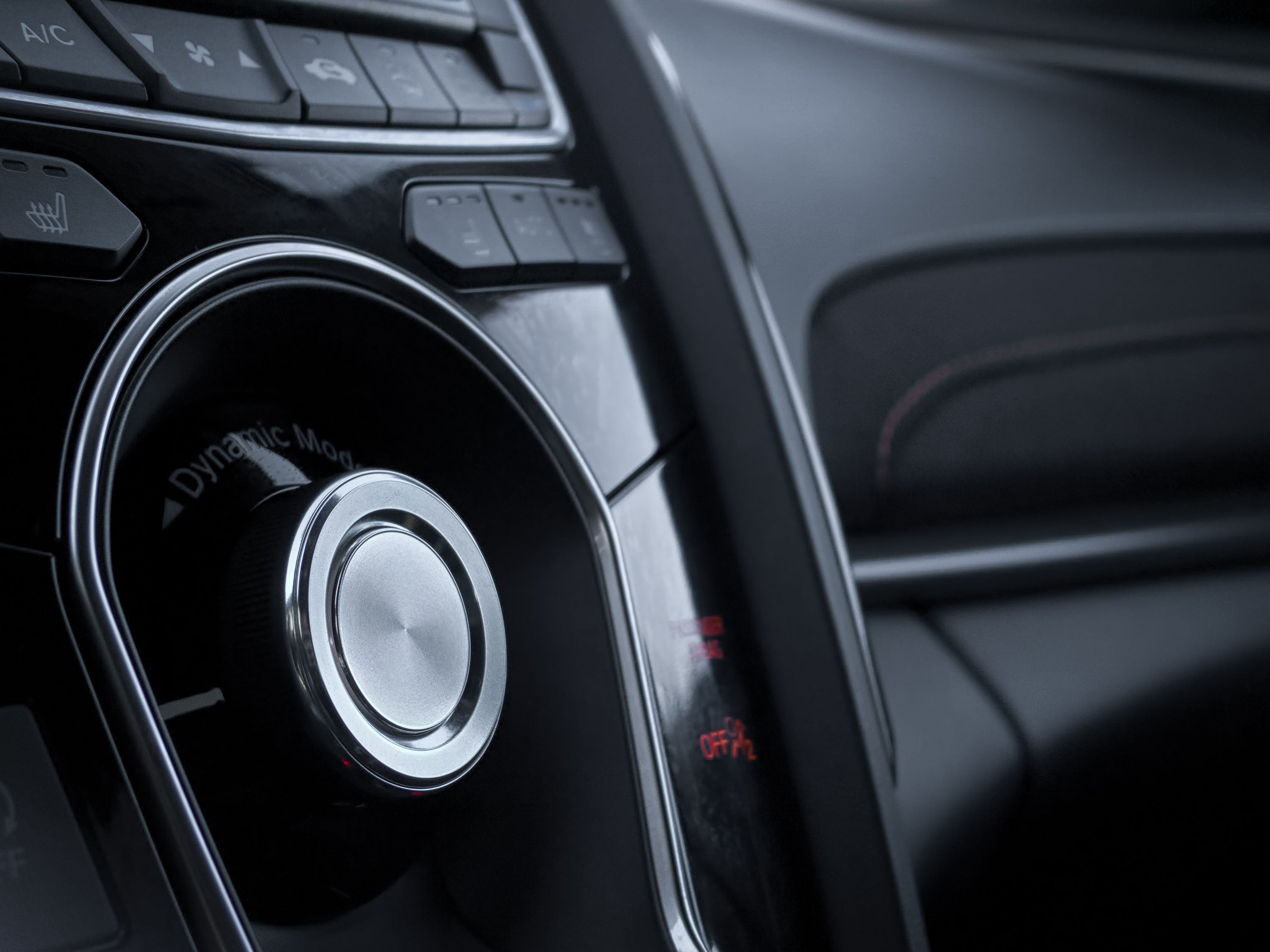 A close-up of a car's control panel featuring a "Dynamic Mode" knob and various function buttons.