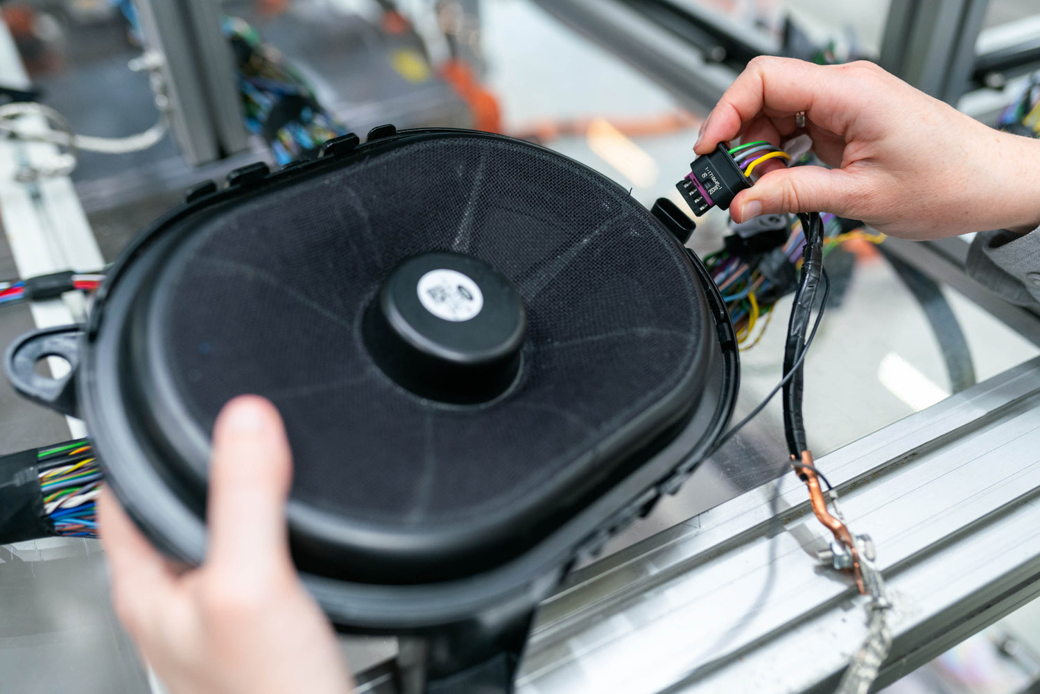 Close-up of hands connecting a wiring harness to a car speaker on an assembly line