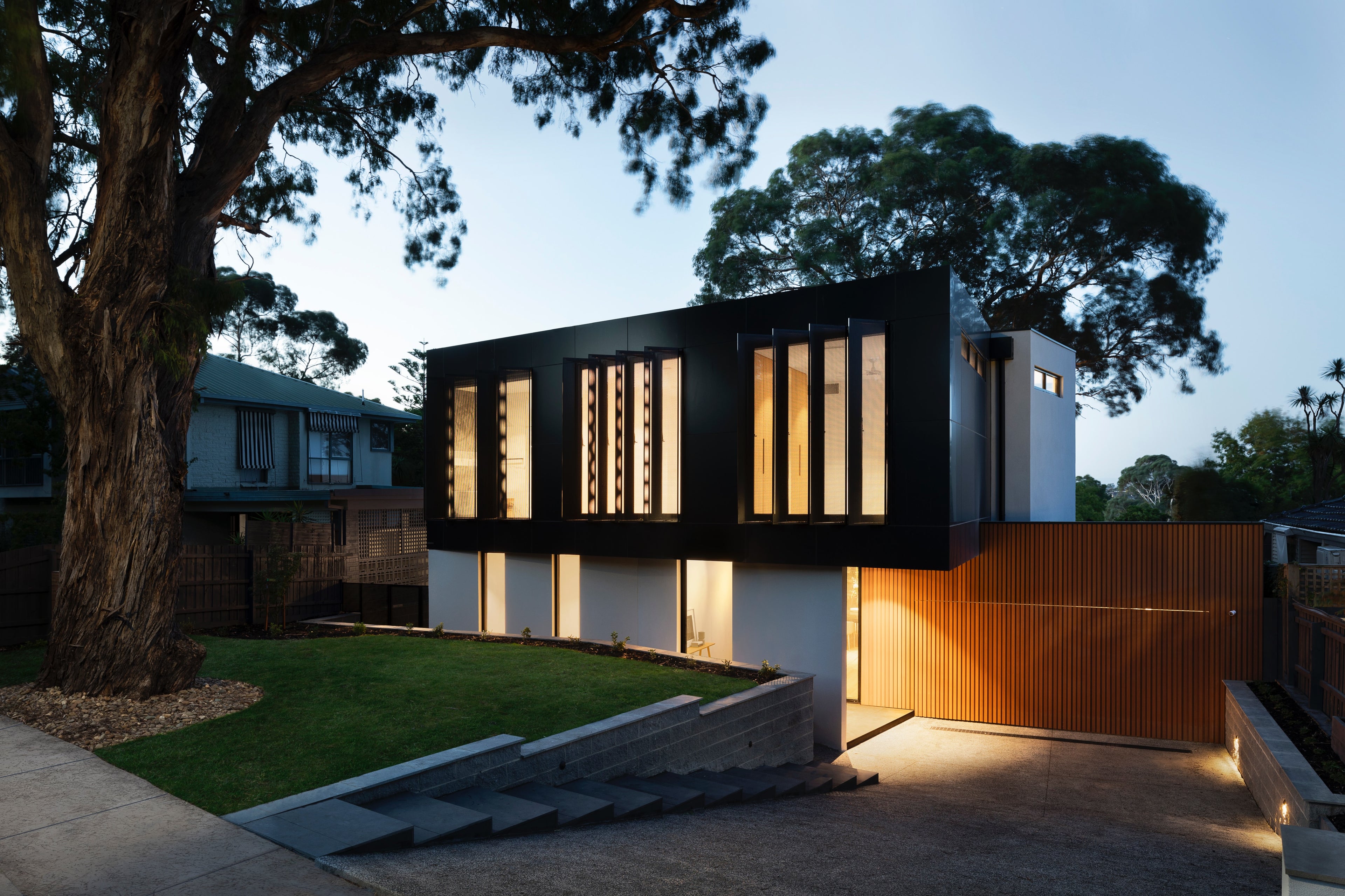 A modern house at dusk with illuminated windows and a wooden gate.